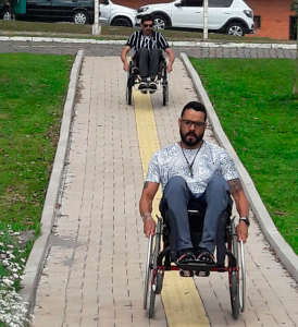 Dois homens participantes do Programa de Habilidades em Cadeira de Rodas empinando suas cadeiras de rodas descendo uma ladeira.